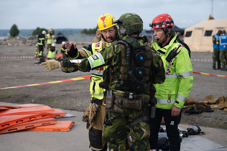 Två befäl från räddningstjänsten står och pekar och diskuterar med en militär