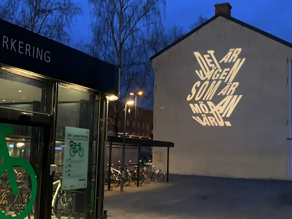 Ljusprojektion på en husvägg vid Cykelställlet med budskapet: "Det är vägen som är mödan värd" - Karin Boje
