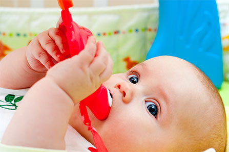 Foto av baby med en leksak i munnen.