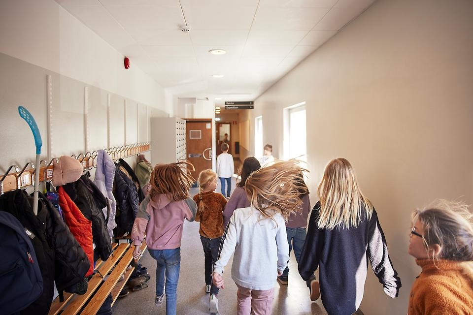 Skolelever springer i korridor.