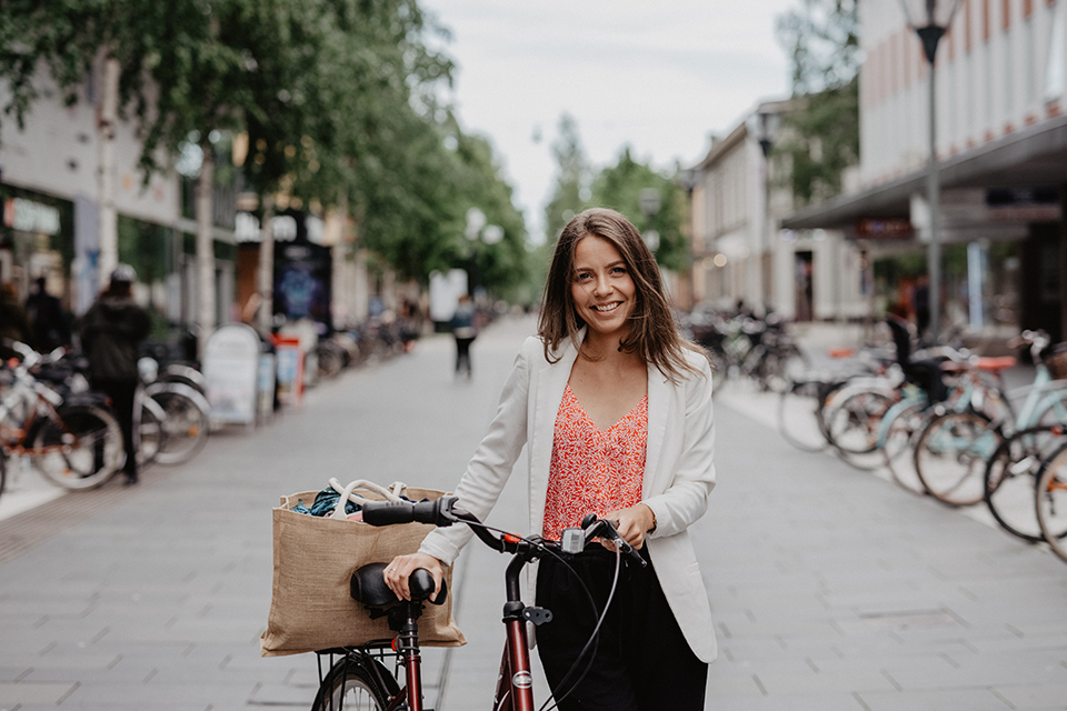 Ung kvinna promenerar med cykel i Umeå centrum.