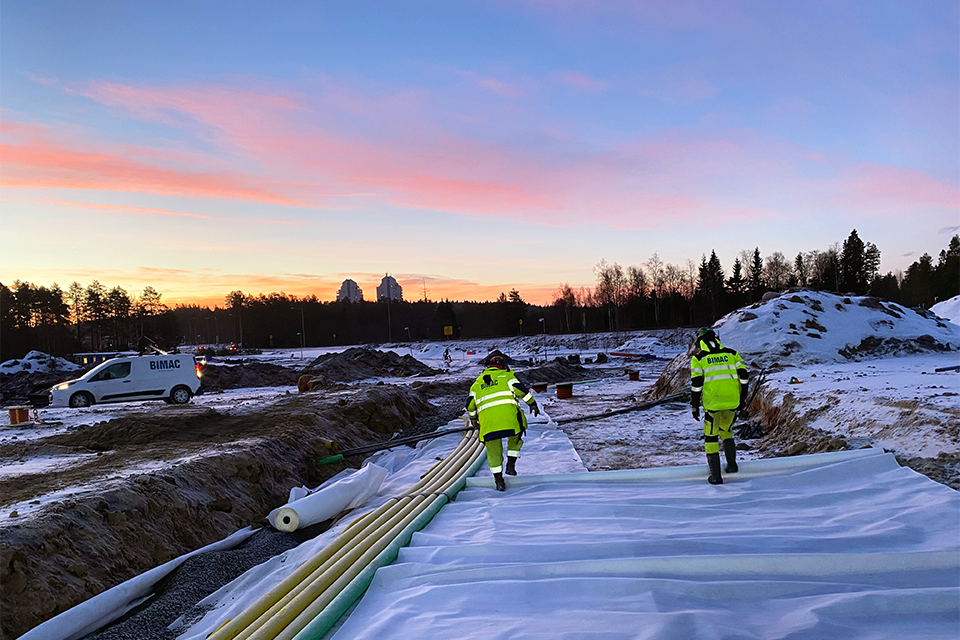 Byggarbetare på byggplats, rosa och blå himmel och snötäckt mark.