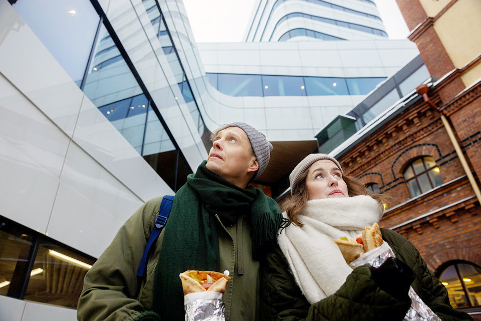 En man och en kvinna står och tittar på Väven med rullpizzor i händerna.