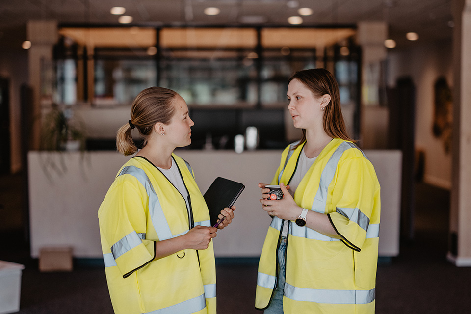 Bilden visar två unga kvinnor som samtalar på jobbet.