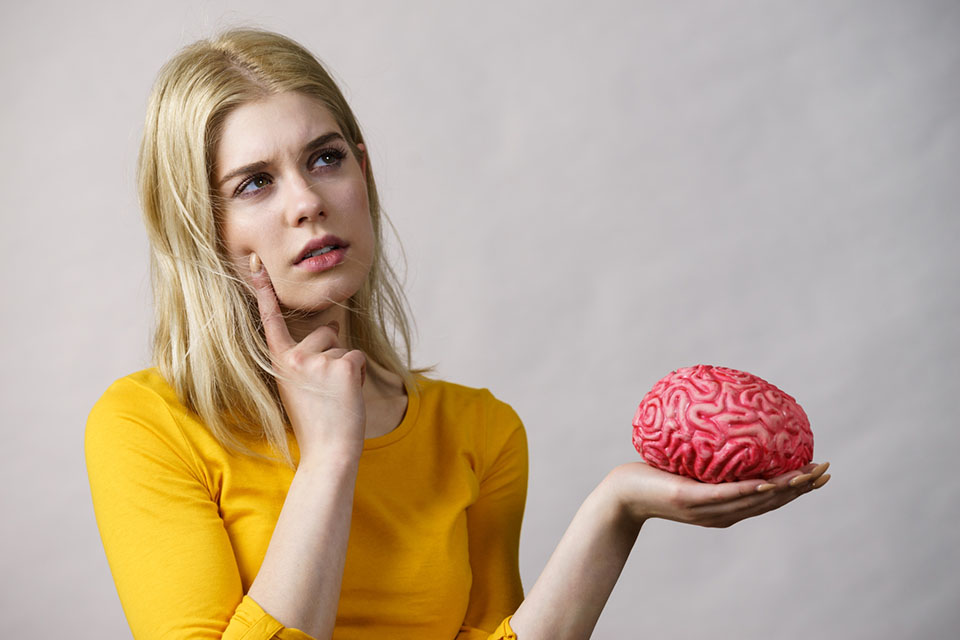 En flicka i gul t-shirt håller en hjärna i handen. Hon ser fundersam ut.
