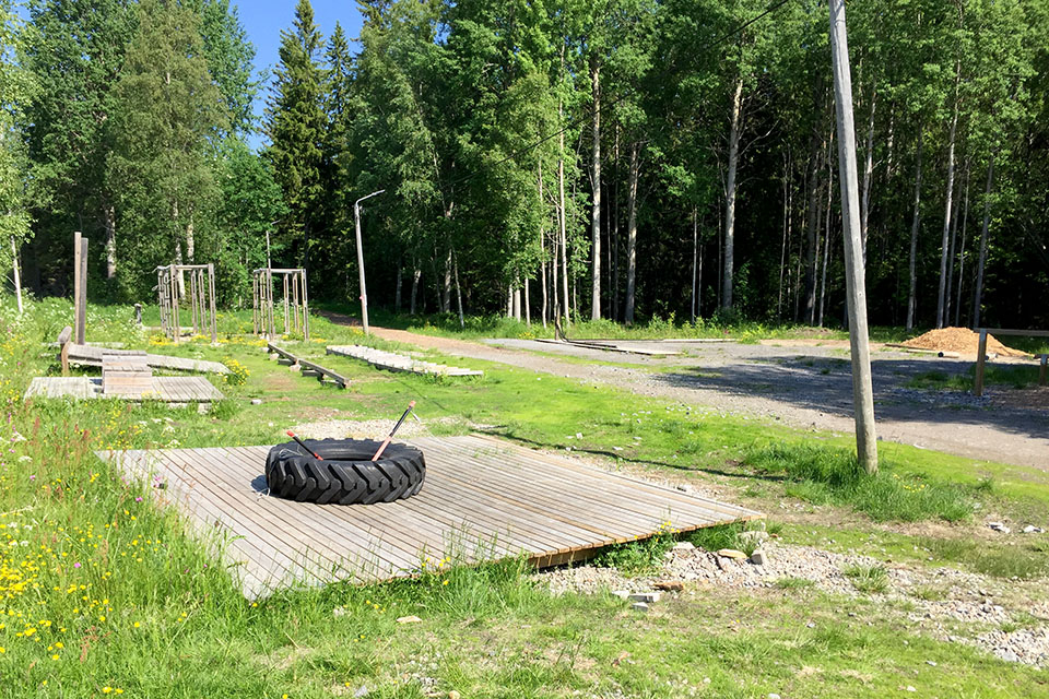 Översikt av ett utegym vid ett skogsbryn med flera olika stationer.