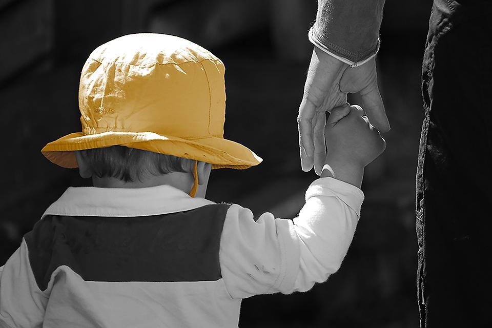 Barn i gul hatt håller en vuxen i handen.
