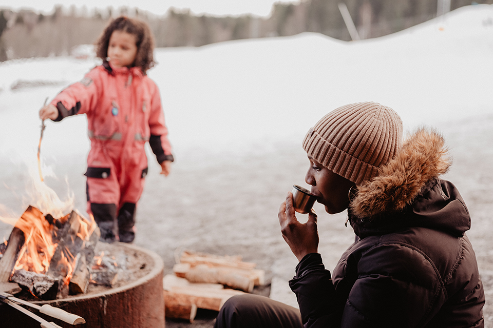 Woman drinking coffee by a fire, child cooking bread in the fire.