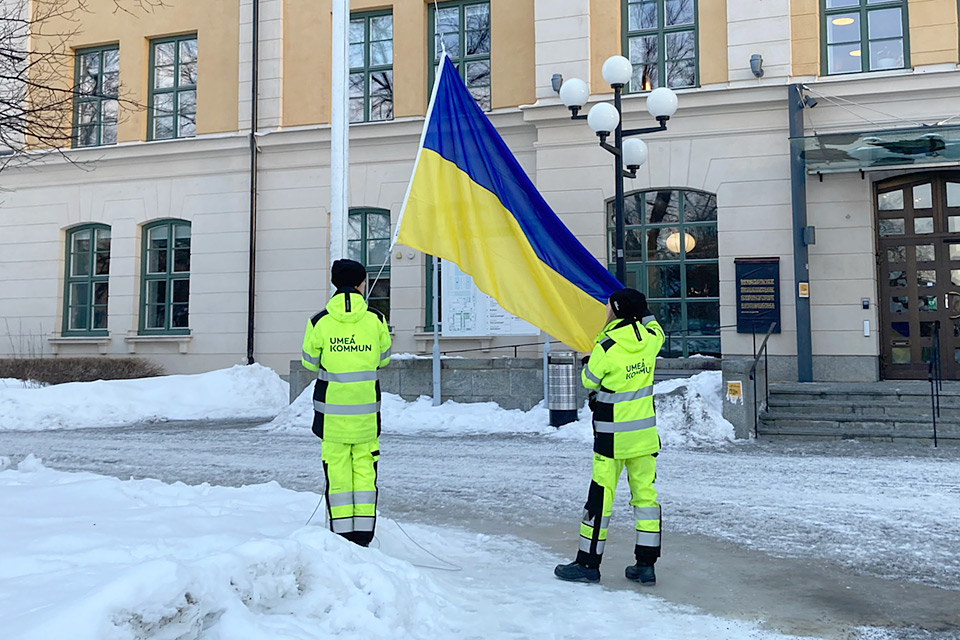 Två kommunmedarbetare hissar Ukrainas flagga vid stadshuset.