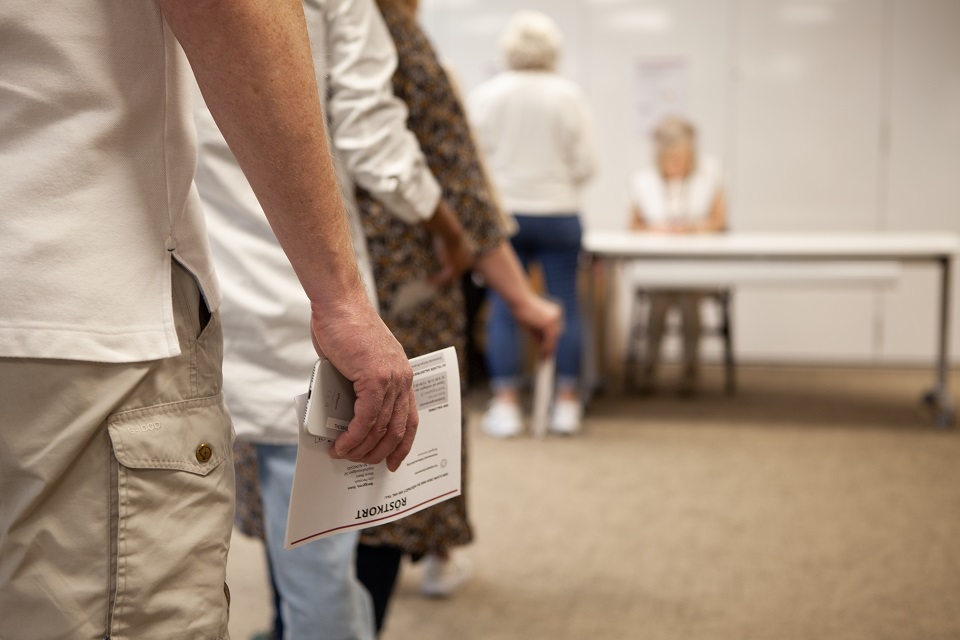Person håller i röstkort och köar för att få rösta