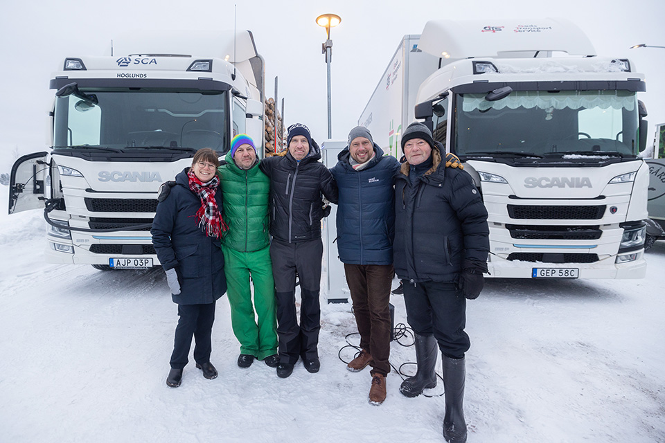 Bilden visar från vänster till höger: Emma Vigren, Johan Lagrelius, Lars Mikaelsson, Hans Lindberg och Donald Näs framför den nya laddstationen och två lastbilar.