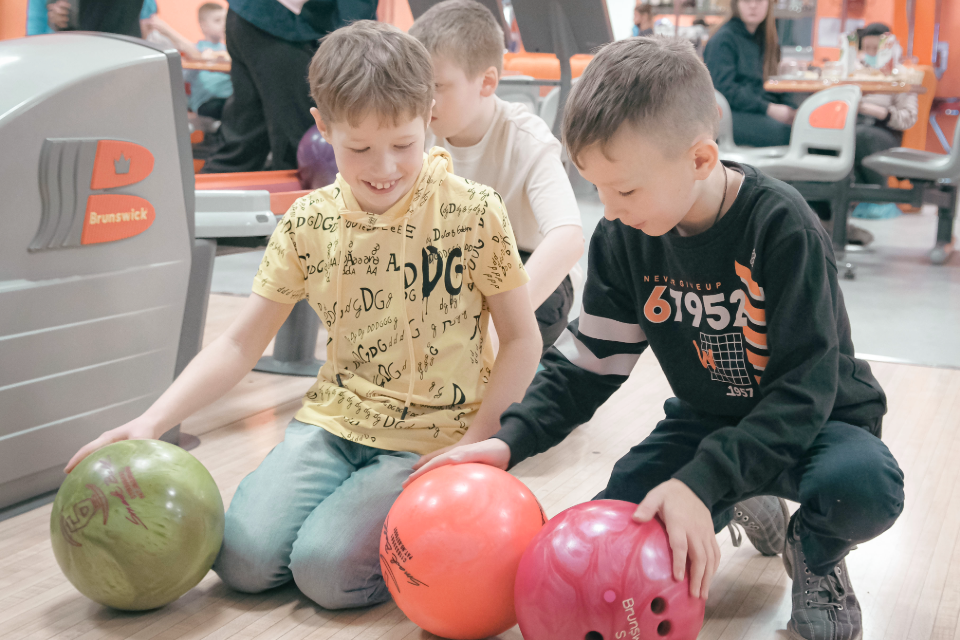 Två barn som sitter på knä med bowlingklot