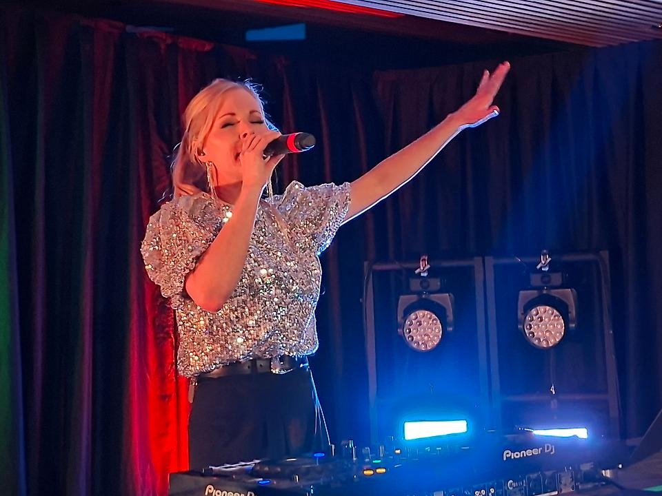 DJ i glittriga kläder på scenen med högtalare i bakgrunden
