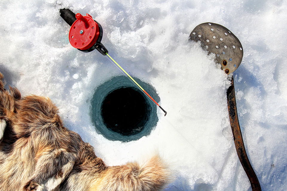 Ett pimpelhål i isen med ett pimpelspö och en spade för att tömma hålet från snö.