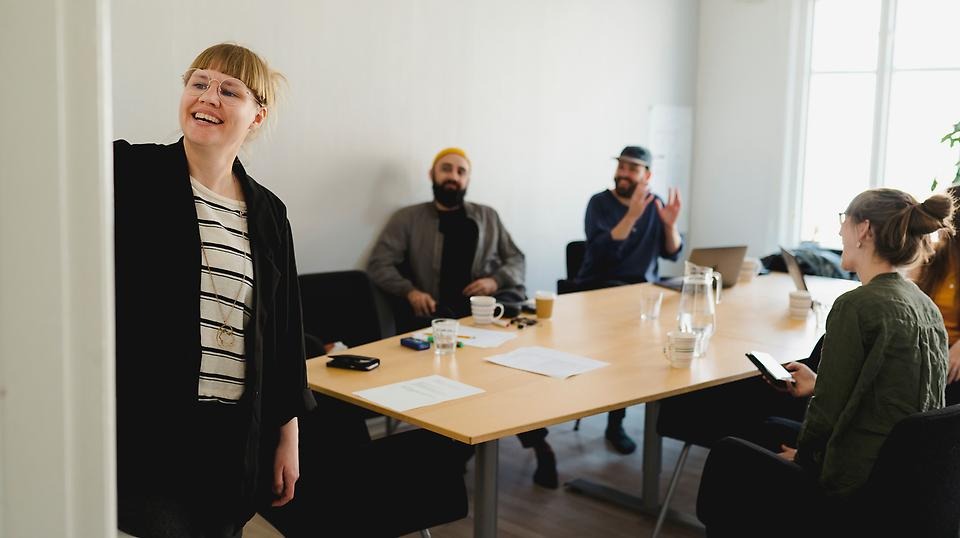 bilden visar fyra pesoner som sitter vid ett bord och lyssnar på en kvinna som skriver på en tavla