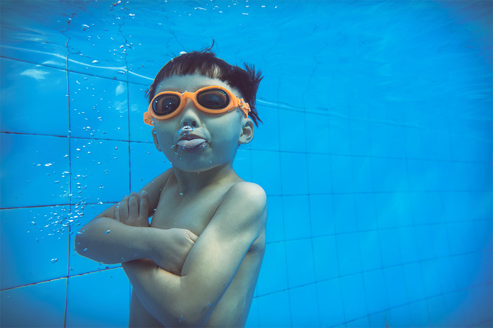 Pojke med simglasögon under vattenytan i en bassäng.