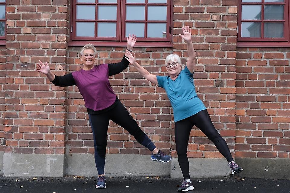 Två glada kvinnor i träningskläder som utför en balansövning.