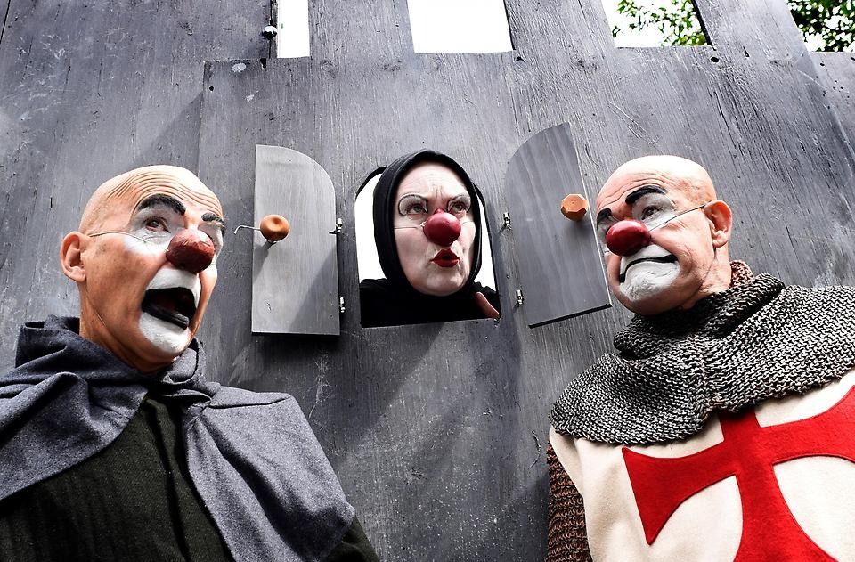Tre män sminkade som clowner med medeltida klädsel, i teaterföreställning utomhus.