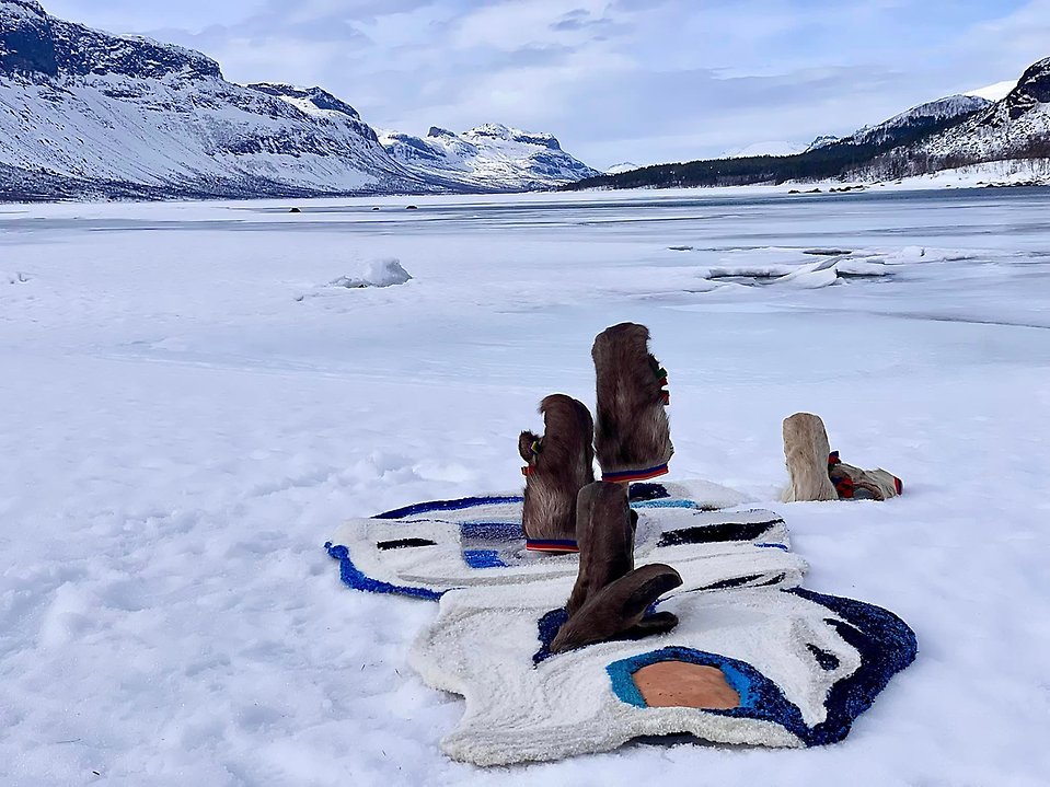 Bild av konstverk bestående av pälssvantar, tuftad matta och renskinn. I bakgrunden ses en fjällvy.