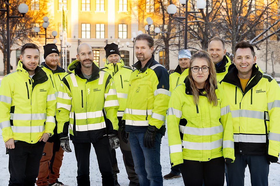 Nio medarbetare på Gator och parker som arbetar med snöröjning och halkbekämpning, i gula varseljackor och framför stadshuset i Umeå