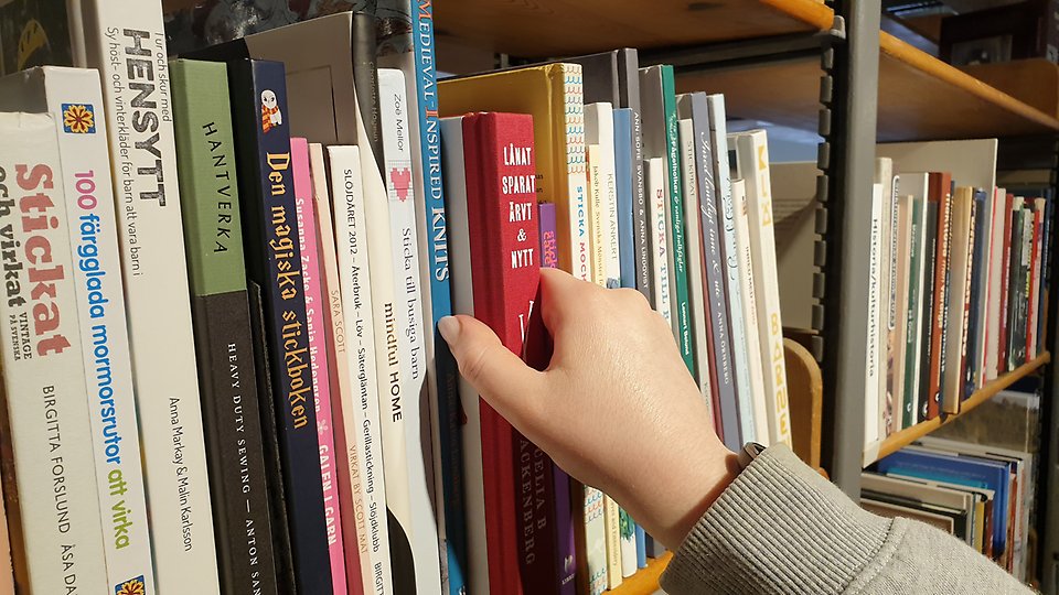 Hand som plochar en bok i en bokhylla. Från KB:s webb 250825