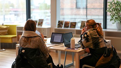 Två unga kvinnor som sitter vid ett bord i biblioteket