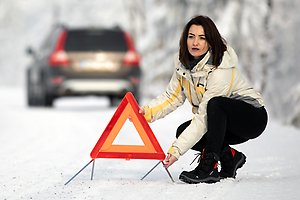 Kvinna sätter ut varningstriangel på vinterväg