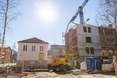Byggarbetsplats med byggkran och fordon- Trävillan Rosa huset till vänster och en ofärdig flygel till vänster blå himmel med starkt solljus.
