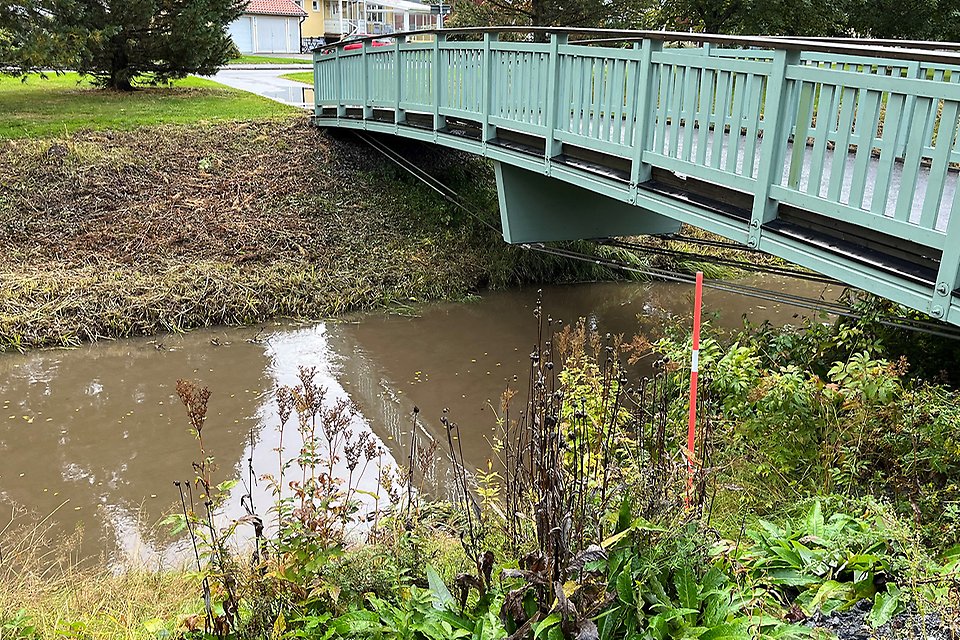 Vattendrag som rinner under en grågrön gångbro.