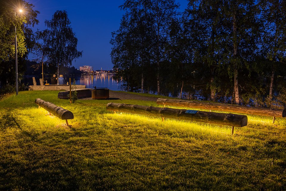 Ett par sitter i kvällsskymningen och blickar ut över Umeå centrum som lyser upp natthimlen i fjärran.
