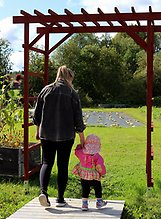 En mamma och ett barn går över en liten bro mot en odling.